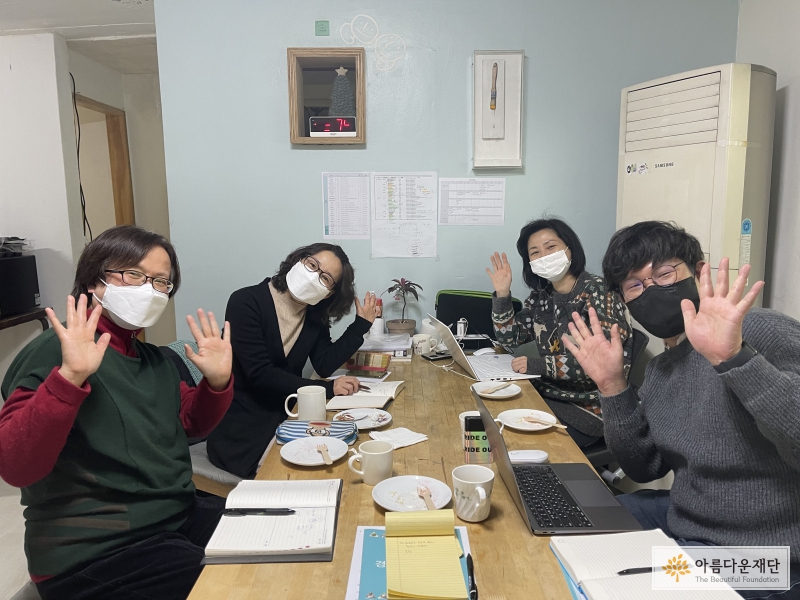 사무작의 사무실 책상 앞에 마스크를 쓰고 앉아 모두 양 손을 펼치며 카메라를 바라보고 있다.