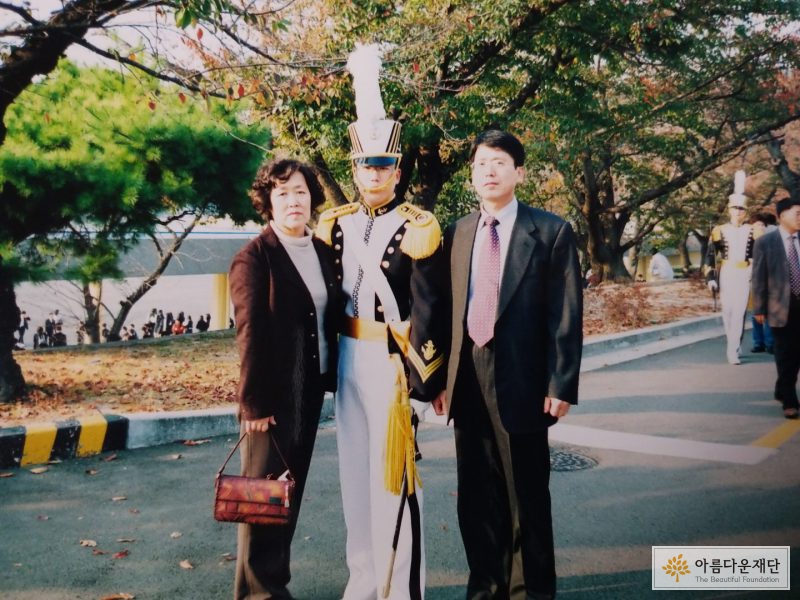 홍창우 기부자가 왼쪽으로는 어머니, 오른쪽으로는 아버지와 함께 해군 장교 임관식 기념 촬영을 하고 있다. 홍창우 기부자는 장교임관예복을 갖춰입고 왼손에는 예도를 차고 가운데 서 있다.