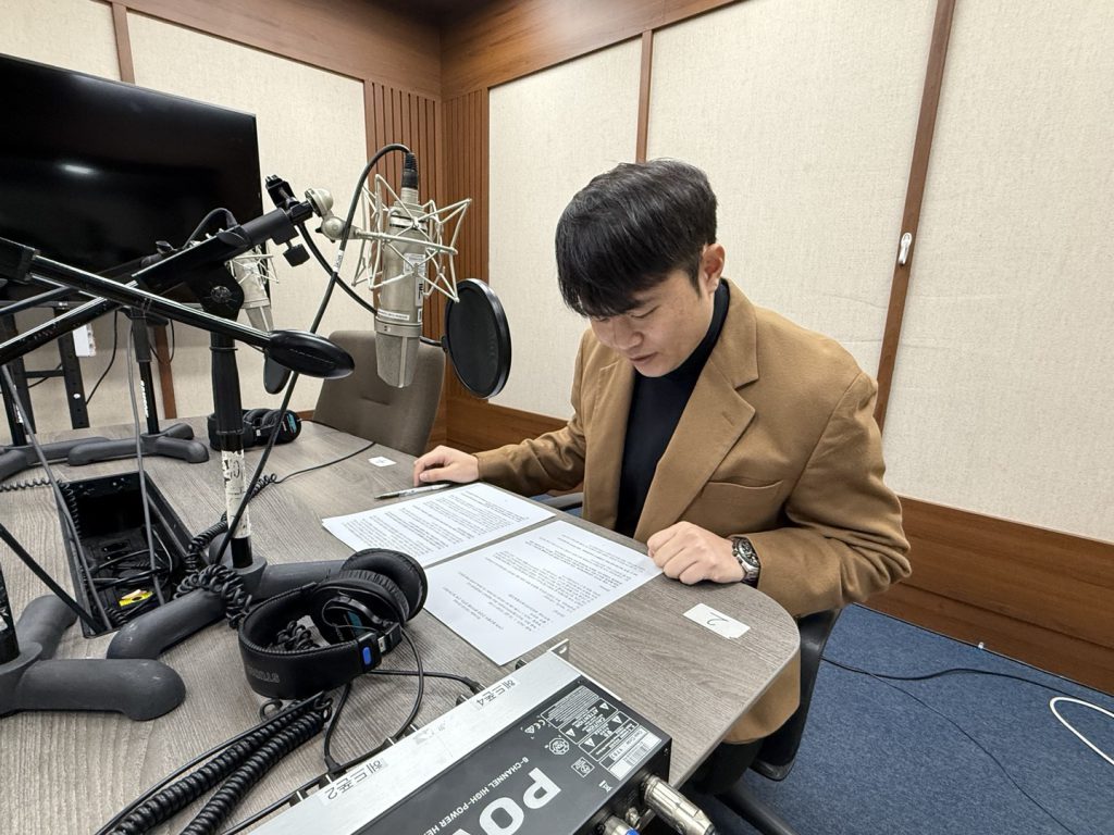 한 남성이 라디오 부스 안에서 원고를 읽고 있다.