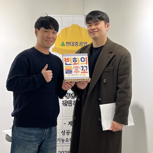 두 명의 남성이 변화의물꼬 입간판을 들고 서 있고, 뒤편에는 현대중공업이라고 써있는 글자가 보인다.