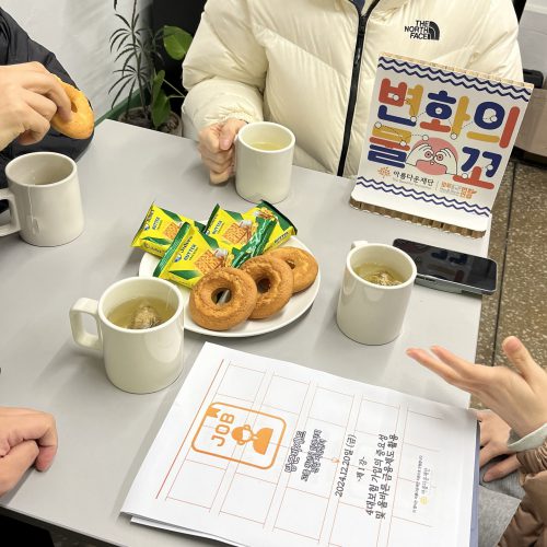 책상에 과자에 차가 놓여있고, 그 주변은 4병의 사람들이 둘러 앉아 있다. 4대보험 가입의 중요성 및 올바른 금융제도 활용이라고 적혀 있는 종이가 책상에 놓여있다.