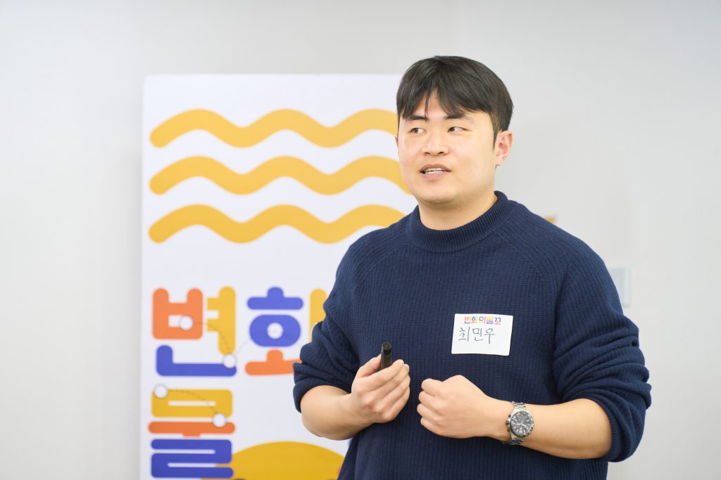 한 남성이 변화의물꼬 입간판 앞에서 말하고 있는 모습