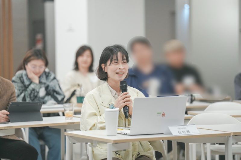 마이크를 들고 한 여성이 웃으며 발언하고 있는 모습, 사진 속 여성은 이 글을 쓴 신아베입니다.