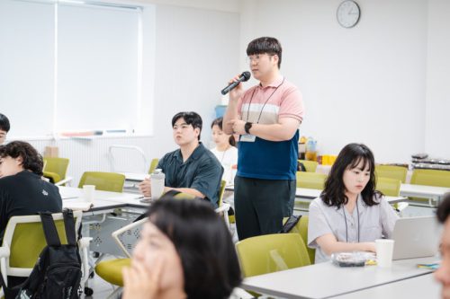 행사 참여자가 테이블에서 일어나 단체 소개를 하고 있다.