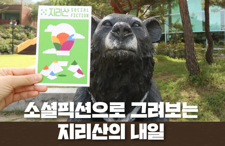 지리산 반달곰 동상 앞에 지리산소셜픽션 엽서가 들려있다. 아래 텍스트는 '소셜픽션으로 그려보는 지리산의 내일' 